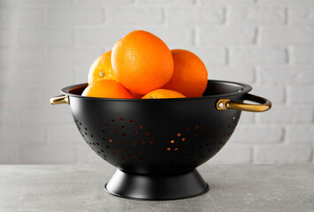 Fresh ripe oranges in black colander on light grey table