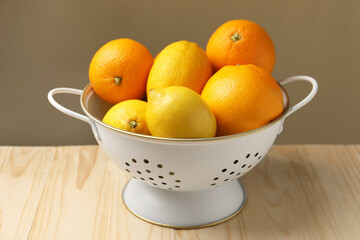 Colander with fresh citrus fruits on wooden table