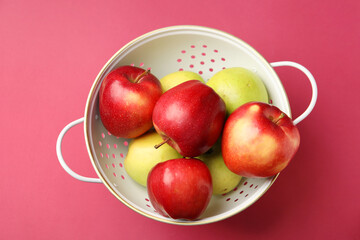 Colander with fresh apples on pink table, top view