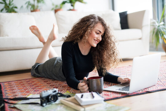 Beautiful woman planning summer vacation abroad, going on trip alone. Lying on floor, working on itinerary on laptop.