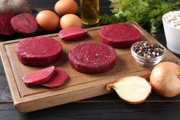 Uncooked beetroot cutlets and ingredients on black wooden table. Vegetarian product