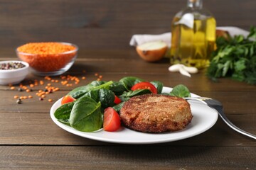 Tasty fried vegetarian cutlet served with spinach and tomato on wooden table
