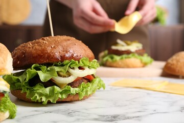 Woman making delicious vegetarian burger at white marble table, selective focus