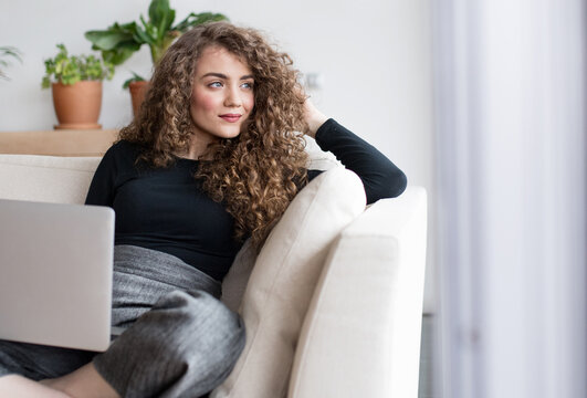 Beautiful woman planning summer vacation abroad, going on trip alone. Sitting on sofa working on itinerary on laptop.