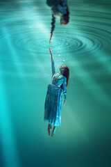 Finding inner self and truth. Poetic underwater scene with elegant young girl reaching out towards distorted reflection on water's surface. Concept of surrealism, beauty, mystery and fantasy, freedom