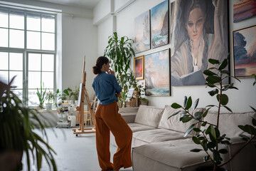 Painter woman looking at painting in artist creative cozy studio. Artist apartment gallery Interior...