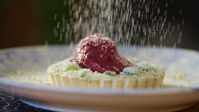 Powdered sugar being poured into grape tart on plate