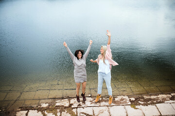 Adult daughter spending time with her mother, having fun, jumping. Mom and daughter outdoors, on...