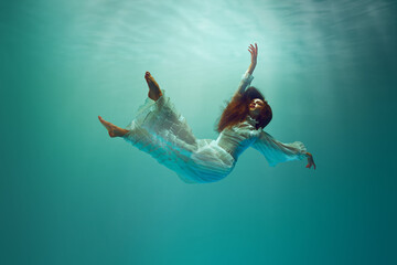 Calm and relaxed young girl in elegant young woman floating in a tranquil underwater environment. Mysterious levitation. Concept of surrealism, beauty, mystery and fantasy, freedom