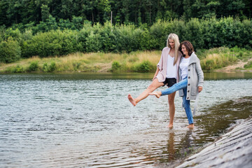 Adult daughter spending time with her mother. Mom and daughter outdoors, walking barefoot in water...