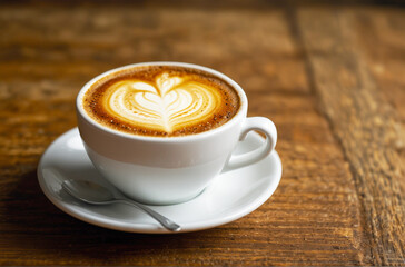 Front view of a glass of cappuccino coffee with painting art on white, creamy foam, on a wooden table