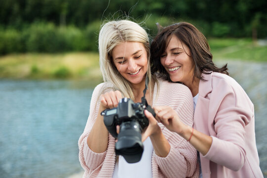 Adult daughter teaching mother how to take photos with professional camera, explaining technology, laughing. Mother's Day concept.
