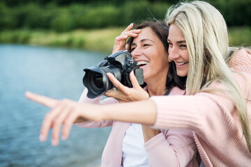 Adult daughter teaching mother how to take photos with professional camera, explaining technology,...