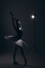 Young ballerina in elegance white tutu and pointe shoes dancing against dark background and...