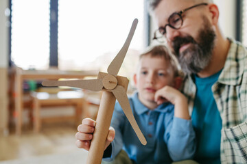 Son and father holding wind turbine model. Concpet of renewable energy sustainable lifestyle for...