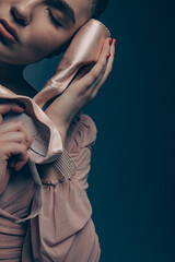 Portrait of young ballerina with closed eyes holding pointe shoes in her hands.