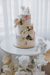 three-story elegant wedding cake on a wooden stand and a white background decorated with rose flowers