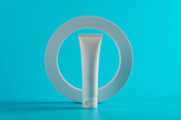 Plastic white tube for cream or lotion. Skin care or sunscreen cosmetic with stylish props on blue...
