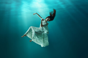 Amazing aquatic scene of elegant young girl lightly floating in the ocean, ocean with sunlight on...