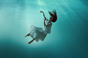 Fairy-like image showing underwater mysterious scene with elegant young girl in tender dress...