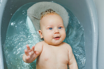 Baby hygiene. The baby lies in the bathtub and bathes. Baby bathing in water.