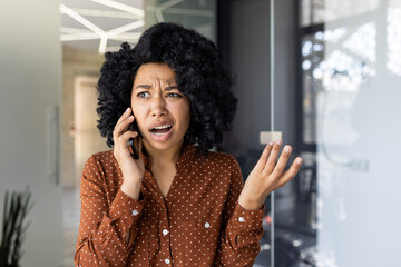 A young Black woman expresses frustration and confusion while talking on a smartphone, conveying...