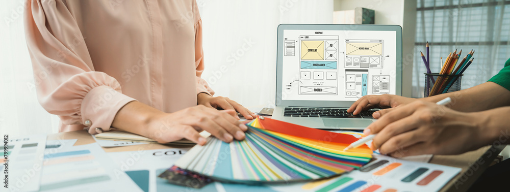 Poster cropped image of interior designer chooses color from color swatches while laptop displayed website 