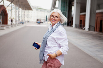 Portrait Happy smiling Senior woman with gray hair in city street wearing fashionable attire white...