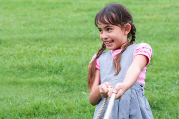 Pretty little girl having fun, playing tug war game pull string at the park
