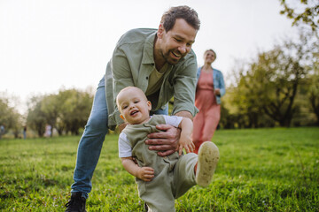 First steps for little toddler. Father supporting baby while walking in soft spring grass on...