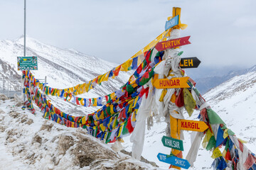 Prayer flags and signpost at the summit of Khardung La pass, at 17,582 feet one of the world's...