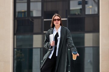 Young successful brunette woman dressed in a black raincoat against the background of a business...