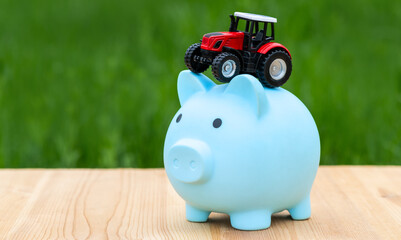 MiMiniature tractor and piggy bank on a background of grassniature tractor and piggy bank on a...
