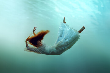 Creative image depicting redhead young calm girl levitating underwater showcasing the harmony of...