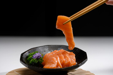 Fresh sliced salmon sashimi served with parsley leaf on a black Japanese style plate