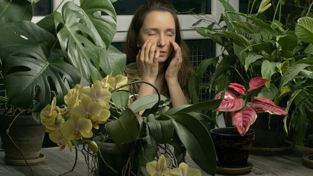 A person practicing EFT in a winter garden with many potted plans on the table. A young woman is sitting among plants and tapping under eye (UE) meridian point. 