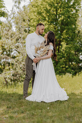 A bride and groom are standing in a field, holding hands and smiling