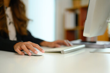 Cropped shot of female manager clicking wireless computer mouse and typing on keyboard