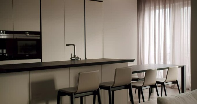 A sleek and stylish minimalist kitchen with integrated appliances and a dining area featuring a long table and stylish chairs, all in soft neutral tones. Modern Minimalist Kitchen and Dining Area