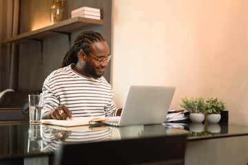 Smiling African American male in casual outfit working on laptop at home