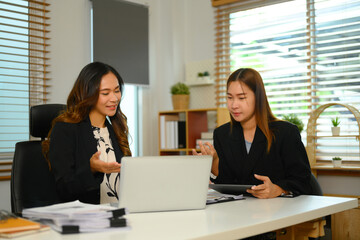 Cheerful young businesswomen using laptop collaborating on new project at office desk