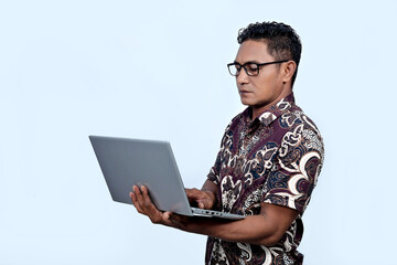 An Indonesian man wearing a batik shirt and working on a laptop