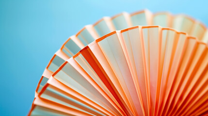 Intricately folded orange paper fan with a soft blue background, highlighting its detailed texture.