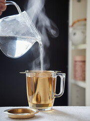 Steaming hot water poured with a transparent jug over a glass cup with a golden filter for...