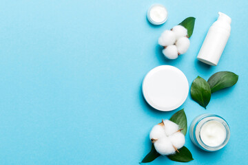 Organic cosmetic products with cotton flower and green leaves on color background. Copy space, flat lay