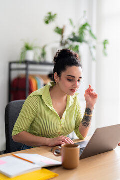 A focused South American woman in a lime-green shirt types attentively on her laptop, a glimpse into daily professional life