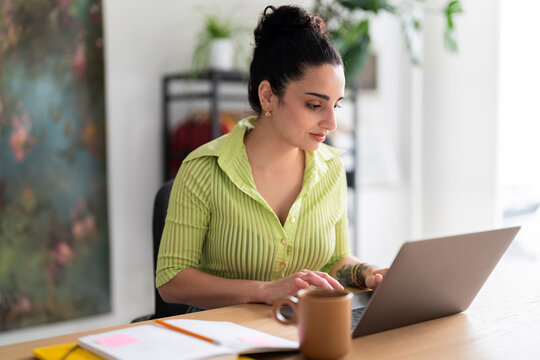 A focused South American woman in a lime-green shirt types attentively on her laptop, a glimpse into daily professional life