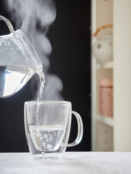 Steaming hot water poured with a transparent jug over a glass cup for infusions or tea.