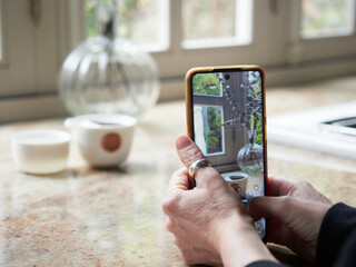 Close up view, female hands holding smartphone taking a photo of a cup on kitchen countertop.