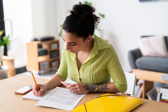 A woman with a thoughtful expression fills out paperwork, attention to detail in a modern home setting